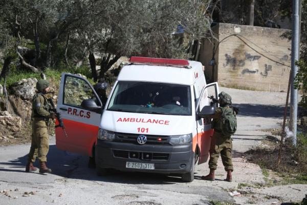Israeli soldiers, with their weapons drawn, block an ambulance, pictured with its doors opened, and search the vehicle.