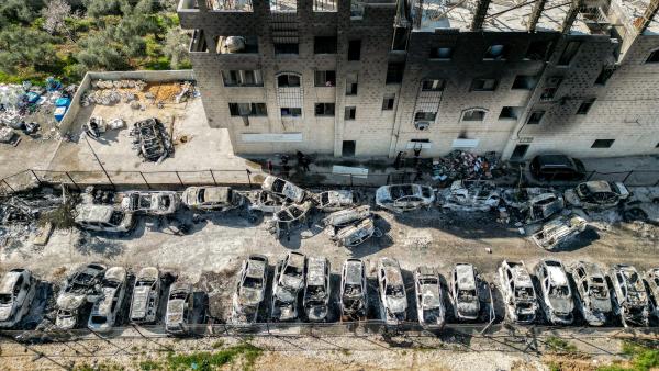 Aerial view of nearly two-dozen cars destroyed by the Israeli settler rampage on the town of Huwara in the West Bank, in addition to burn damage from the flames ignited to burn the cars on a residential home behind the parking lot.