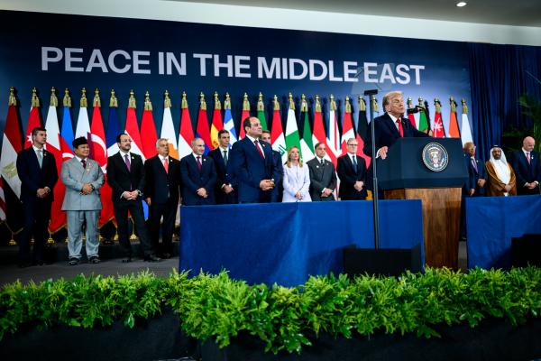 US President Donald Trump addresses the Sharm El Sheikh Summit in Egypt, joined on stage by Egyptian President Abdel Fattah El-Sisi and other world leaders. Behind them are flags belonging to states participating in the summit, and backdrop text reads "PEACE IN THE MIDDLE EAST."
