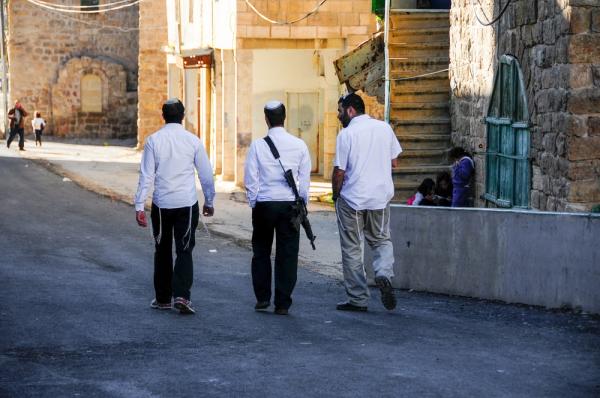 Israeli settlers walk through the streets of Hebron, one carries an assault rifle.