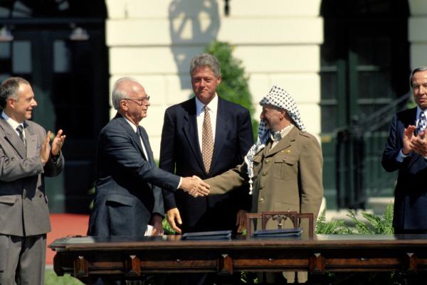 Palestine Liberation Organization (PLO) Chairman Yasser Arafat shakes hands with Israeli Prime Minister Yitzhak Rabin on the White House lawn as President Bill Clinton looks on for the signing of the First Oslo Accord (1993).
