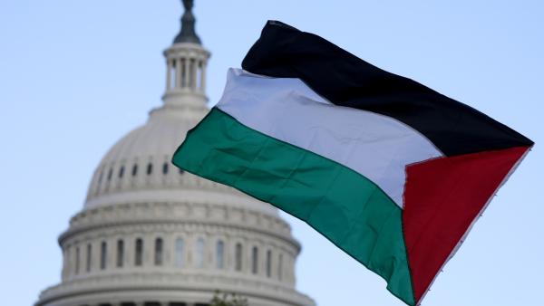 A Palestinian flag waves in the foreground, with the dome of the Capitol building in the background.