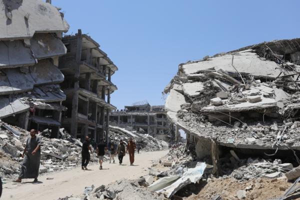Palestinians walk between heavily damaged buildings on either side of the road in Zawayda, a town in the Deir al-Balah Governorate of the Gaza Strip. June 2024.