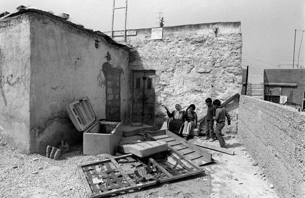 A Palestinian woman and children sit at their home, destroyed by the Israeli military, in the West Bank's Kalandia refugee camp, 1985.