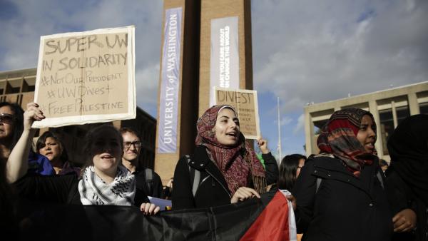 Students and faculty protest President-elect Donald Trump at the University of Seattle, Washington. One holds a Palestinian flag. A sign reads "SUPER UW IN SOLIDARITY #NOTOURPRESIDENT #UWDIVEST #FREEPALESTINE.