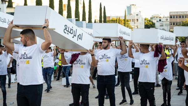Palestinian citizens of Israel protest the Israeli government's inaction against crime impacting their community, they carry symbolic coffins describing the victims of such violence. In Arabic, one is labeled "mother to an infant."