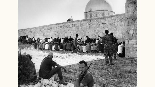 Israeli soldiers line up Palestinian and Jordanian prisoners of war against a wall in Jerusalem, the top of the Dome of the Rock is visible behind the wall..
