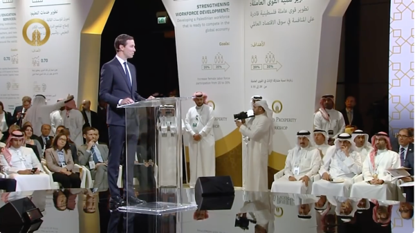 Jared Kushner speaks at the Peace to Prosperity Workshop. The walls display graphics and text communicating the goal of the Kushner plan. One heading reads "strengthening workforce development."