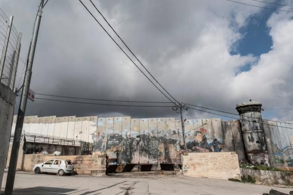 Image of Israel's apartheid wall with graffiti of the Palestinian struggle, including Palestinian with a slingshot and a blindfolded Palestinian being arrested by Israeli soldiers.