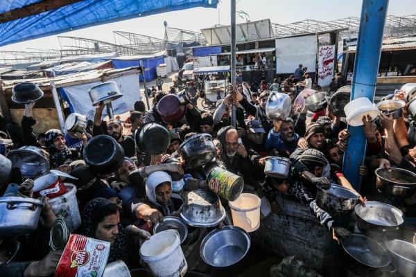 A large crowd of Palestinians carry pots, large cans, and large bowls and reach out for food from a meal distribution center as Israel's forced starvation of the Gaza Strip intensifies. January 2025.