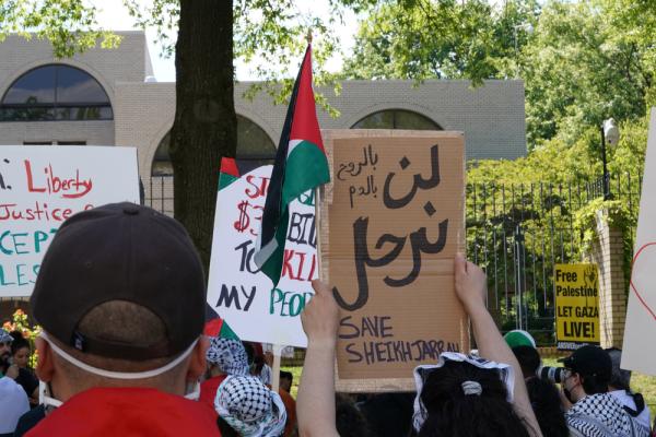 Protestors rally outside of the Israeli Embassy in Washington DC, carrying signs and flags. One bi-lingual sign reads "with our souls, with our blood, we won't leave" in Arabic and "SAVE SHEIKH JARRAH" in English. May 2021.