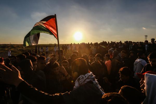 A large crowd of Palestinians  participate in Gaza's Great March of Return at the Israel-Gaza border fence east of Rafah, at sunset, as a Palestinian flag waves in the crowd. March 8, 2019.