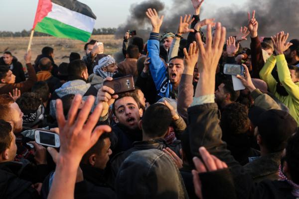 A large crowd of Palestinians participate in Gaza's Great March of Return at the Israel-Gaza border fence east of Rafah. Smoke rises in the background, as some protestors take photos and videos on their phones. January 25, 2019.