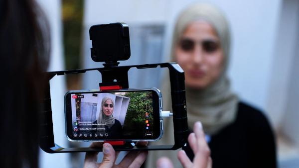 Mona el-Kurd is pictured through the mobile live stream on a reporter's phone, with the recording of El Kurd in the foreground, as she stands in the background and addresses the media after her release from an Israeli police station in Jerusalem. June 6, 2021.