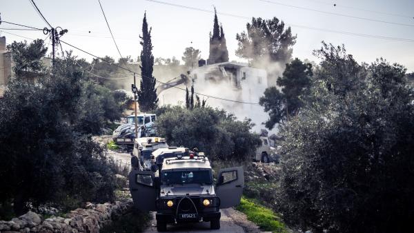 Israeli military vehicles guard as construction equipment demolishes Palestinian homes in the West Bank.