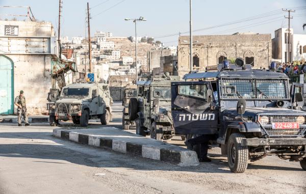 An Israeli military police jeep, and two military jeeps in the streets of the old city of Hebron, as soldiers patrol on foot.