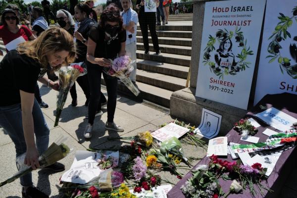 Mourners place flowers at a memorial for Shireen Abu Akleh as part of the Nakba commemoration in Washington DC in 2022, just weeks after she was shot and killed by Israeli forces in Jenin. A poster with her image says "Hold Israel accountable for shooting journalist Shireen, 1971-2022." A symbolic casket is placed on the ground, adorned with flowers, a kuffiyeh, and artwork honoring Abu Akleh.