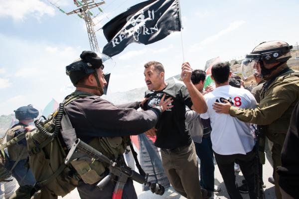 A Palestinian waving a flag bearing the word "RETURN" in English, is physically pushed back by an Israeli soldier as part of a Nakba protest in the West Bank. May 14, 2013.