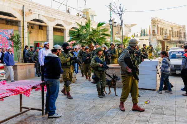 A large crowd of Israeli soldiers carrying weapons, including one attack dog, guard a group of Israeli settlers walking through the Palestinian city of Hebron in the West Bank.