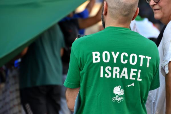 Image focuses on back of a protestor's shirt, which says "Boycott Israel" with a graphic of a missile headed towards a baby carriage.