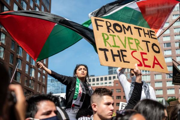 Protest against Israel's 2021 war on Gaza outside of the Israeli Consulate in Boston. Two protestors wave Palestinian flags, one holds a sign that says "FROM THE RIVER TO THE SEA."
