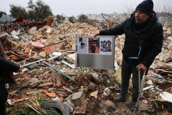 A Palestinian man carries his crutches in one arm, and a poster in support of the Salhiya family of Jerusalem's Sheikh Jarrah neighborhood, on the ruins of their home, demolished by Israel.