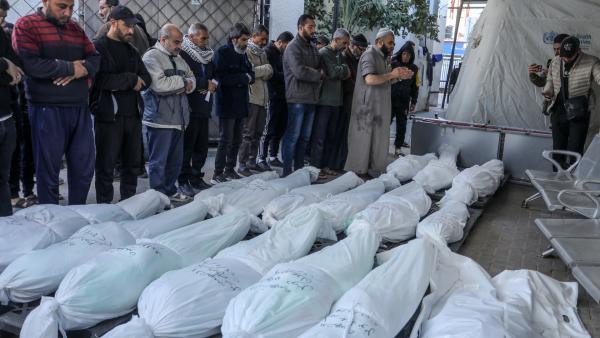 Palestinians perform funeral prayers for victims of an Israeli airstrike on the grounds of Al Najjar Hospital in Rafah. Sixteen victims in burial shrouds, with their names and identifying information hand-written in black ink on the shrouds, are featured in this image.