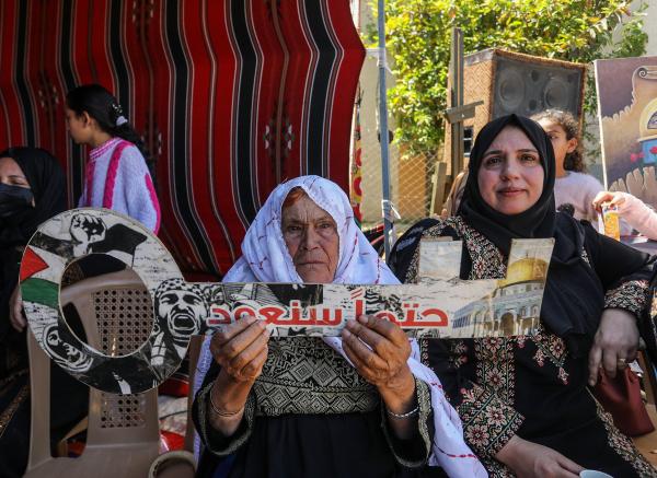 A Palestinian elderly woman holds a sign in the shape of a key, a symbol of the Palestinian right of return to their original homes, that says in Arabic: "inevitably, we will return."