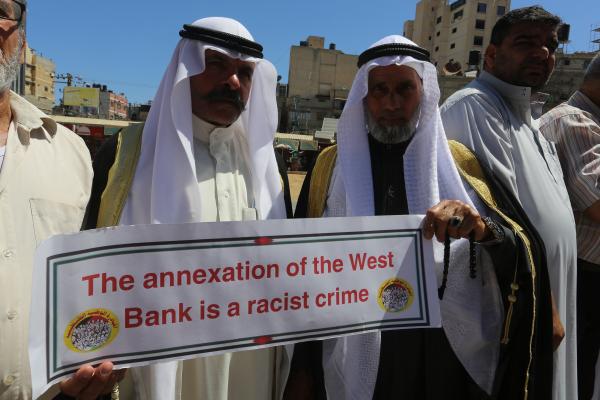 Palestinian protestors carry a sign that says "the annexation of the West Bank is a racist crime."