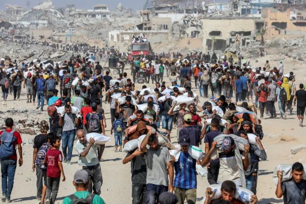 A large crowd walks from to and from a humanitarian aid distribution site near the Zikim, some carry sacks of flour..