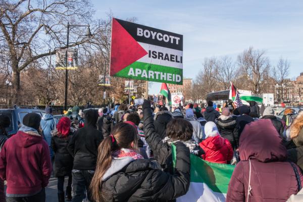 Protestor carries a sign that says "Boycott Israeli Apartheid" over the Palestinian flag, a sign in support of the BDS movement.
