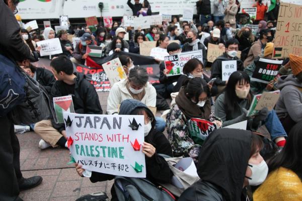 Protestors carry signs in Japanese and English demanding a ceasefire in Gaza. One prominent sign reads "JAPAN STANDS WITH PALESTINE" in English. Shibuya, Tokyo, Japan.