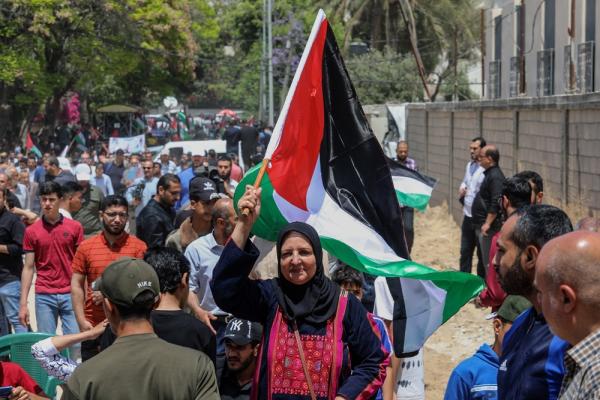 At a rally commemorating the 74th anniversary of the Nakba, a Palestinian woman wearing a traditional thobe waves a Palestinian flag.