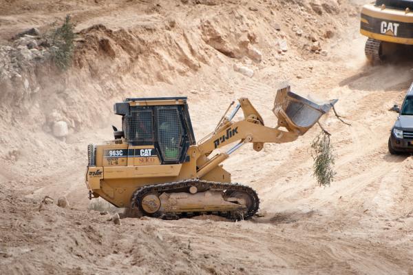 Israeli soldiers operate a weaponized Caterpillar bulldozer in the West Bank, carrying an uprooted branch of an olive tree in the Palestinian village of Al-Walaja in the West Bank.