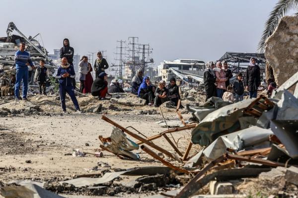Displaced Palestinians returning to their homes in Gaza City stand on the road amid the ruins.