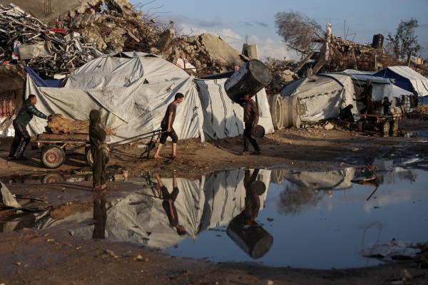 Palestinians walk past makeshift tents and high piles of rubble as they pull firewood and carry supplies in the aftermath of heavy rain and flooding in Gaza.