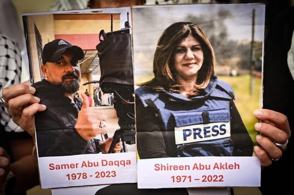 At a vigil, an attendee holds up memorial signs for Samer Abu Daqqa (1978-2023) and Shireen Abu Akleh (1971-2022), two Palestinian journalists assassinated by Israel
