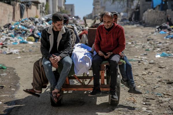 The body of a victim of Israel's Flour Massacre, wrapped in burial shrouds, is pulled on a donkey cart alongside mourners.