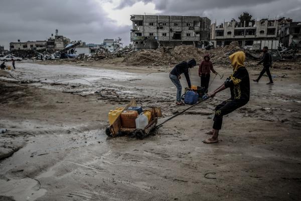 Palestinians drag heavy water bottles under difficult conditions amid the ruins in Khan Yunis, Gaza.