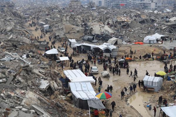 Aerial view of heavily destroyed buildings in the Jabalia refugee camp in Gaza image depics Palestinians under tents and selling goods in harsh outdoor winter conditions.