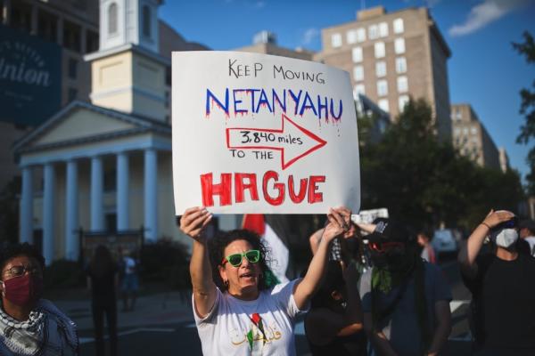 Protestor in Washington DC holds a sign that reads "KEEP MOVING NETANYAHU, 3,840 miles TO THE HAGUE."