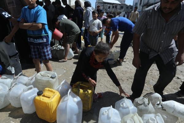 A young girl and other displaced Palestinians fill jerrycans with water in the midst of a severe water shortage.