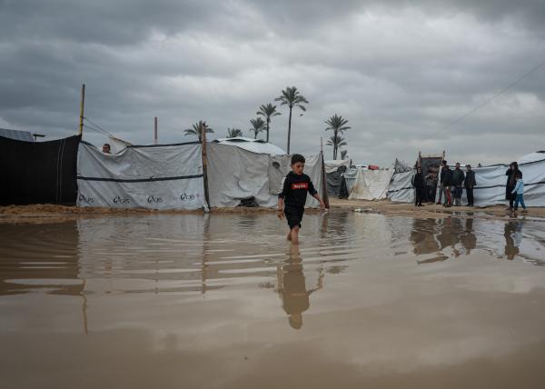 A Palestinian boy walks through a high puddle left from severe flooding in Gaza near displacement tents where Palestinians struggled to endure harsh winter conditions.