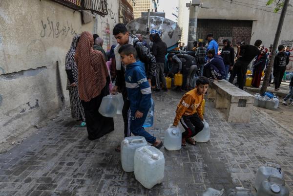 Palestinians fill jerrycans of water as they wait in long lines for limited water resources. Children are pictured helping their families carry and secure water.