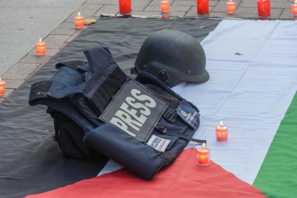 RSF vigil for Palestinian journalists held in Logroño, Spain, featuring a press vest and helmet over a Palestinian flag surrounded by candles.