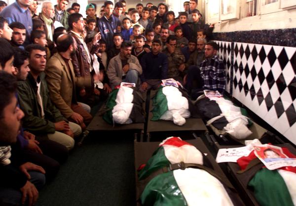 Mourners perform funeral prayers for five Palestinian boys who were killed by an Israeli tank shell ordnance in the Khan Yunis Refugee Camp. Their burial shrouds are draped in Palestinian flags, with photos of each child. November 2001.
