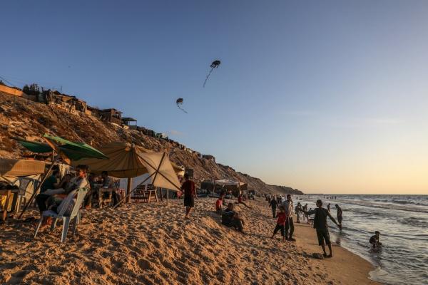 Palestinians enjoy a beach day, some children fly kites.