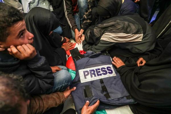 Family members, friends, and colleagues mourn over the body of Hassan Aslih, a Palestinian journalist assassinated in a targeted Israeli airstrike. He is draped in a Palestinian flag, with his press jacket on top.