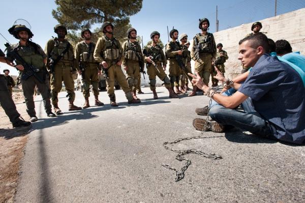 West Bank Palestinians protest with symbolic chains around their wrists in solidarity with Palestinian prisoners in Israeli jails as Israeli soldiers look on. 