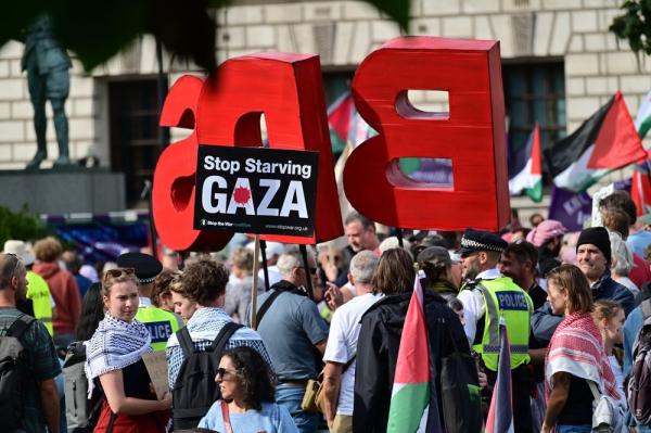 At a rally in London, a protestor holds a sign that says "Stop Starving Gaza" as others carry Palestinian flags and extra large letters that read "BDS."
